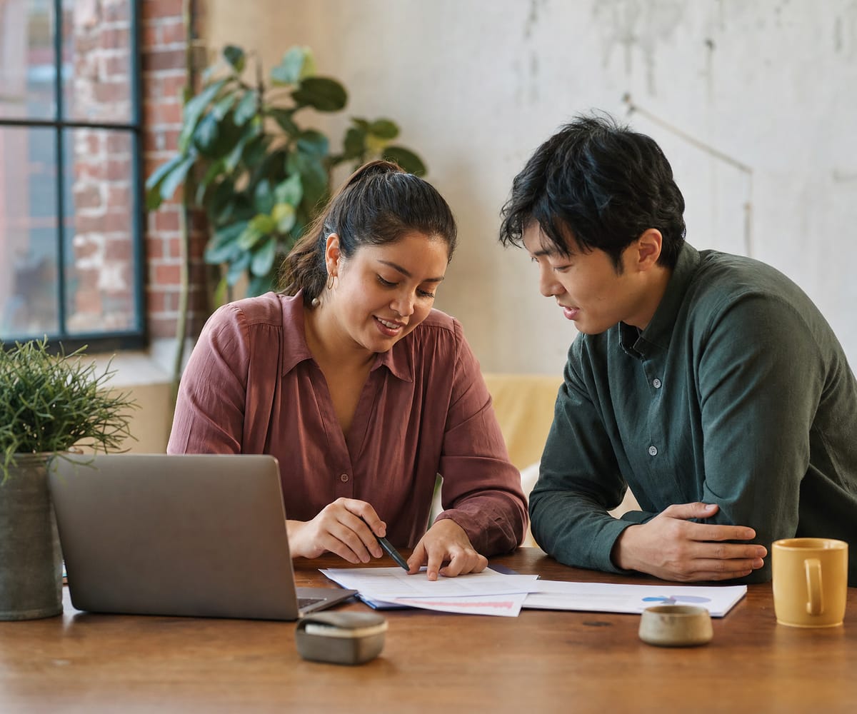 Two co-founders reviewing a printed budget at a shared workspace table